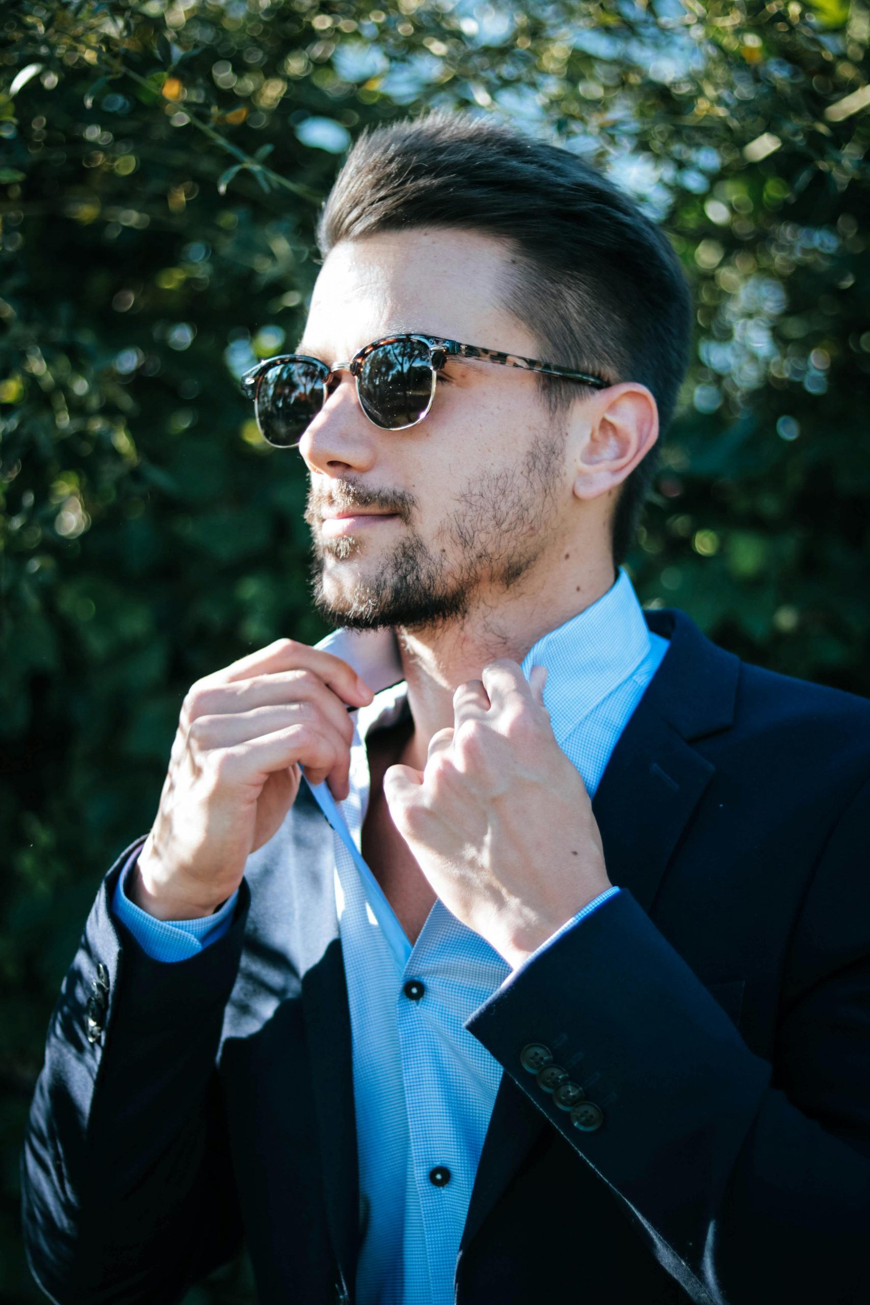 Home Fashionable man adjusting his suit and sunglasses outdoors on a sunny day.